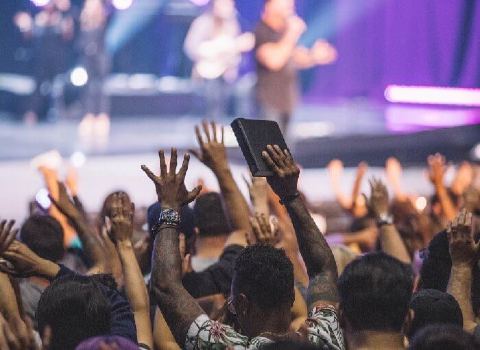 Un culte protestant bondé avec des gens levant les mains en l’air.
